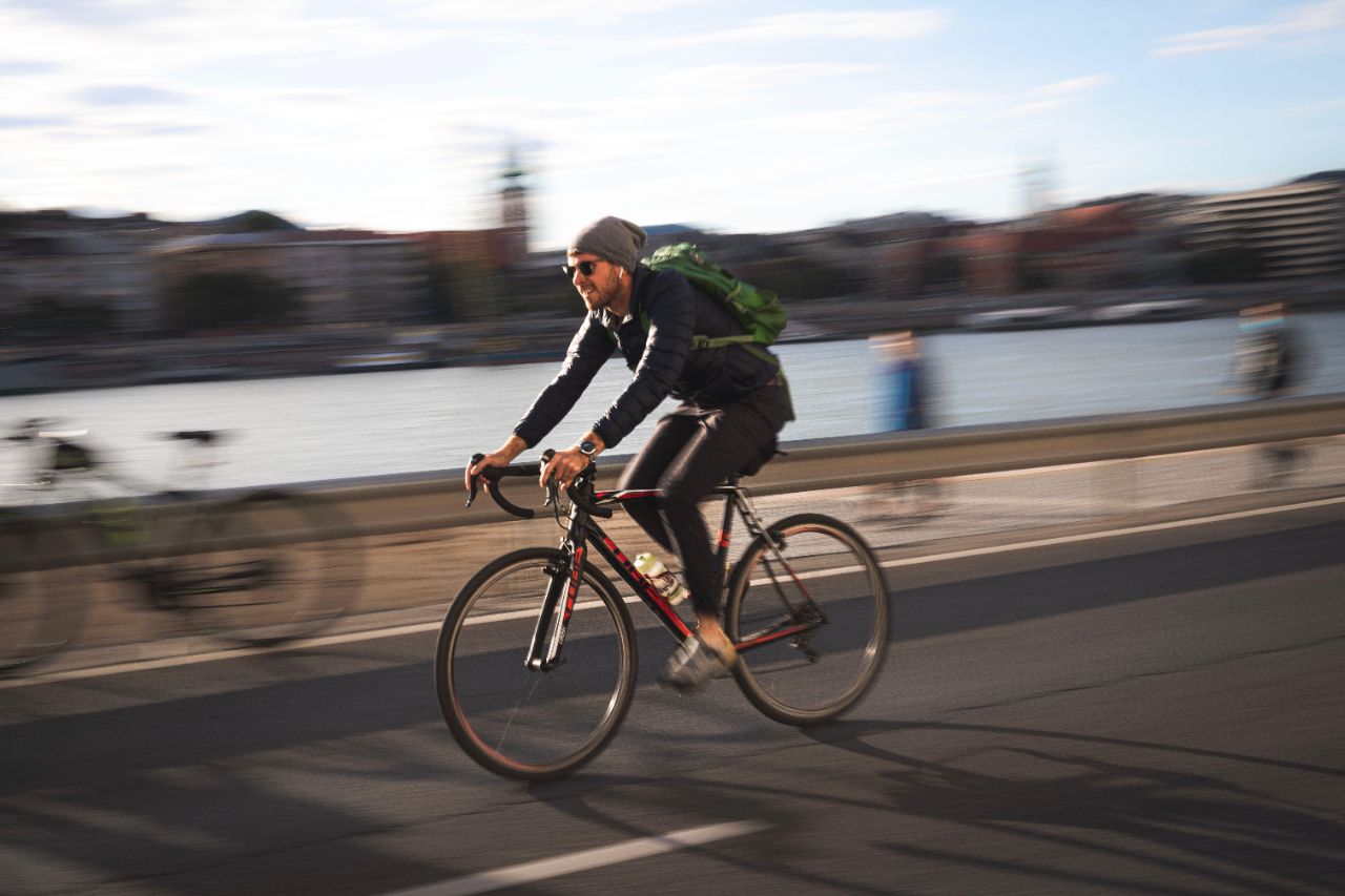 Ein Mann mit Jacke, Mütze und Rucksack fährt auf seinem rot-schwarzen Fahrrad durch die Stadt