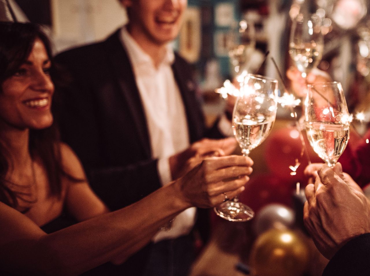 Ein paar Freunde feiern Silvester, stoßen mit Sektgläsern an und halten eine Wunderkerze in der anderen Hand