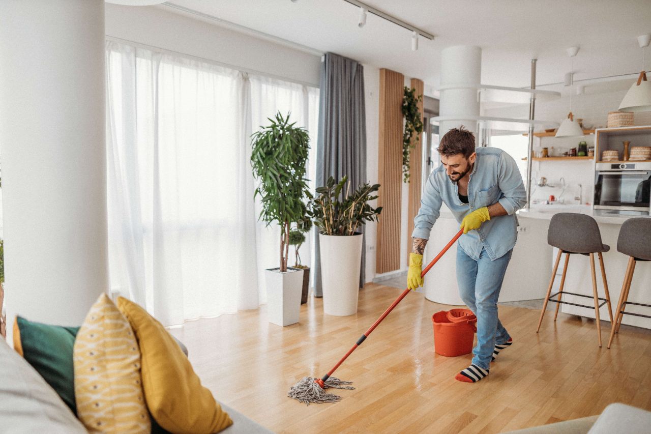 Mann wischt mit einem Wischmopp den Laminatboden in der Wohnung