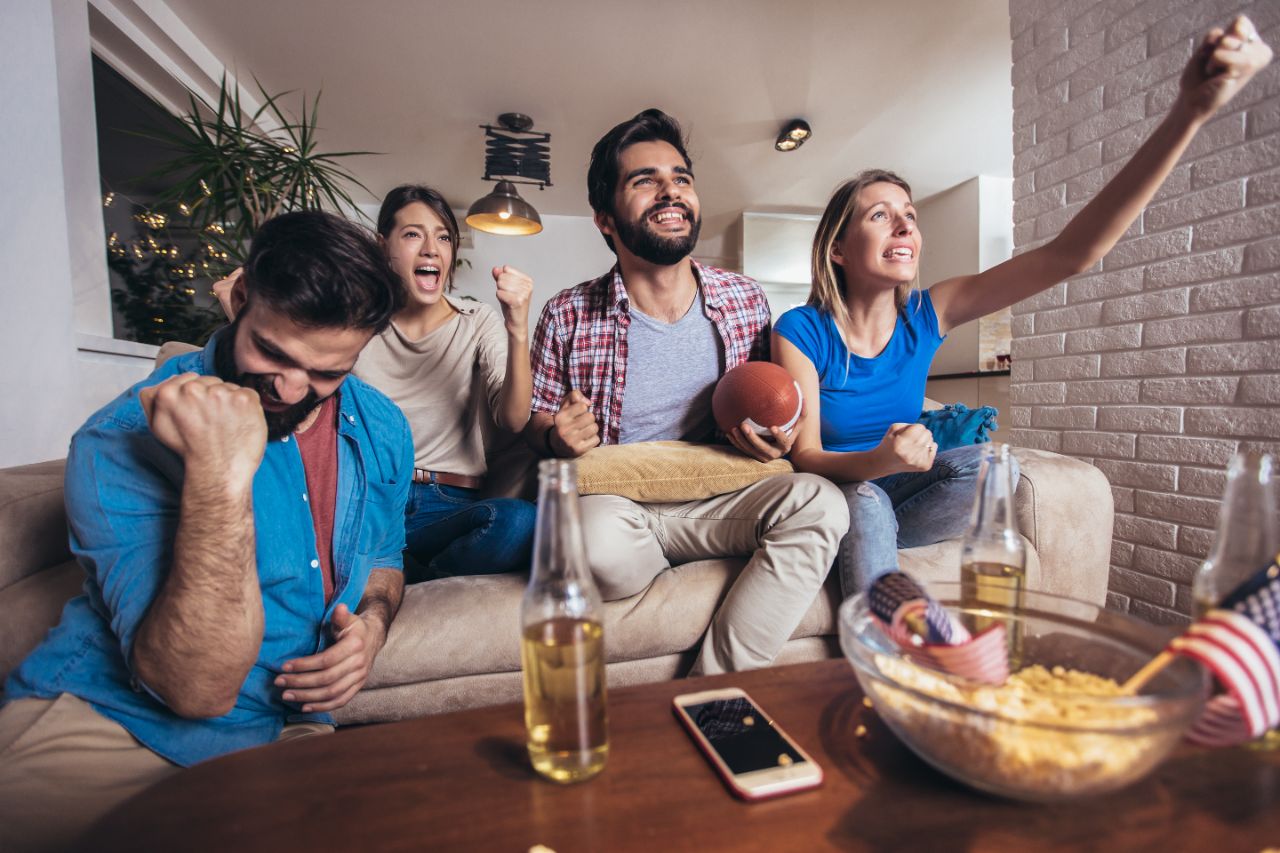 Vier Freunde sitzen jubelnd auf der Couch und schauen sich zusammen ein NFL Spiel an